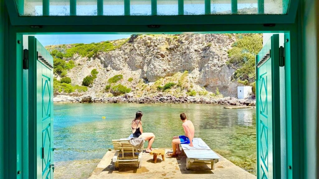 Relaxing by the crystal-clear cove, viewed through open turquoise doors—an intimate escape into nature’s calm
