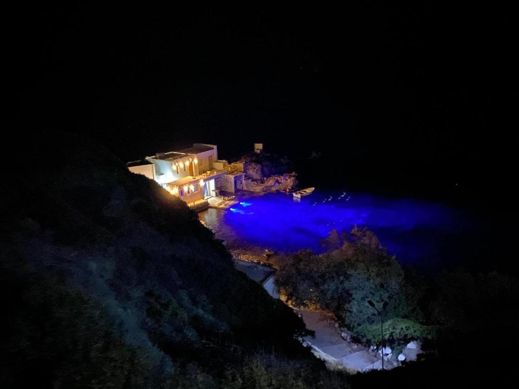 Secluded coastal villa glowing at night with blue-lit waters and peaceful cliffside surroundings