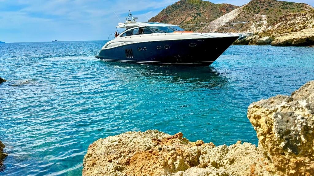 Luxury yacht anchored in turquoise waters near rocky cliffs and coastal hills