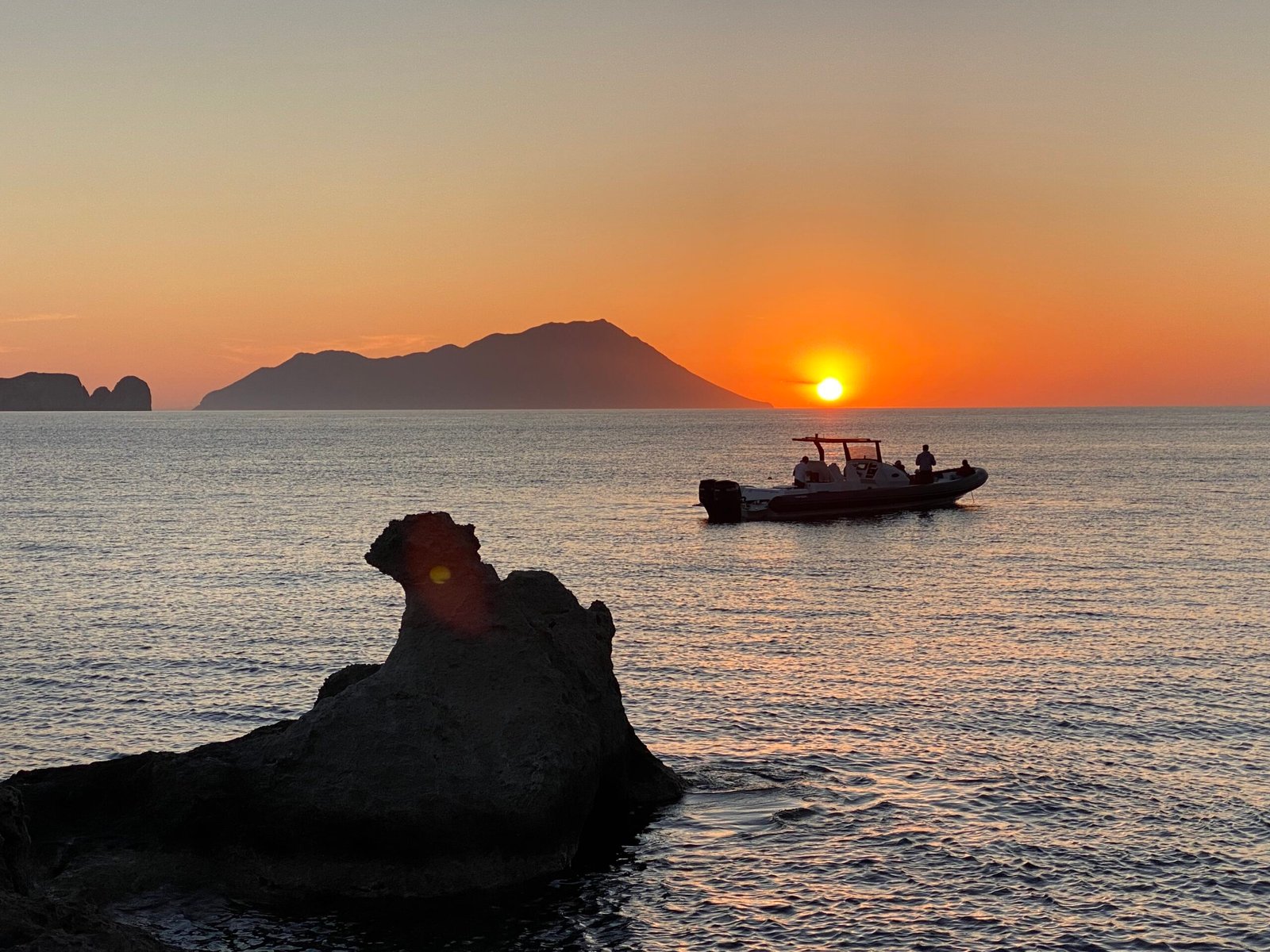 Scenic sunset over calm waters with a boat and silhouette island in the horizon