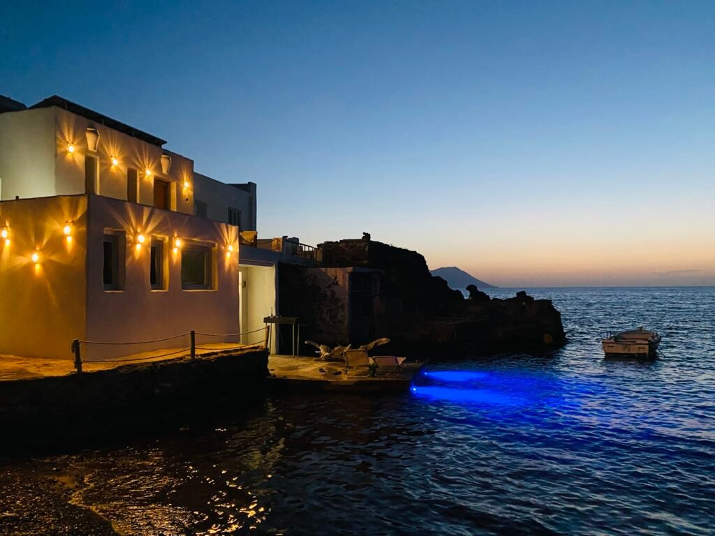 Seaside house glowing at dusk with a blue-lit boat and a peaceful ocean view