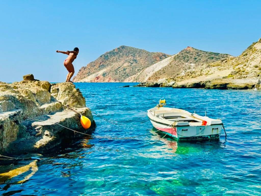 Person preparing to dive into a vivid blue cove with boat nearby